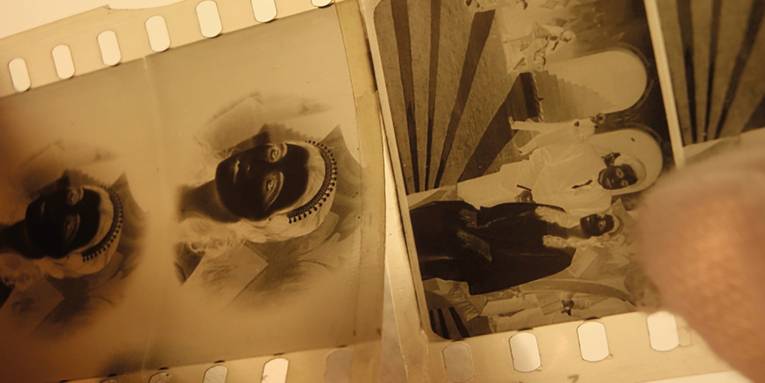 Das Foto zeigt drei Bilder eines 35-Millimeter-Filmnegativs. Rechts unten sieht man einen Daumen der Hand, die den Streifen bei der Restaurierung hält.